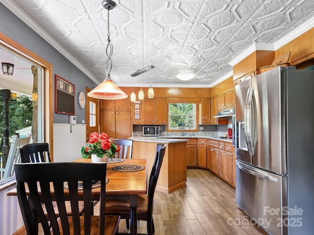kitchen with brown cabinets, stainless steel appliances, light wood-style floors, an ornate ceiling, and hanging light fixtures