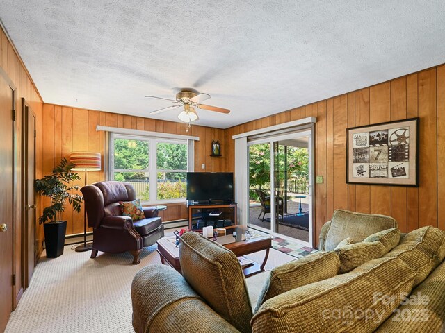 living room featuring a ceiling fan, light carpet, wood walls, and a baseboard heating unit