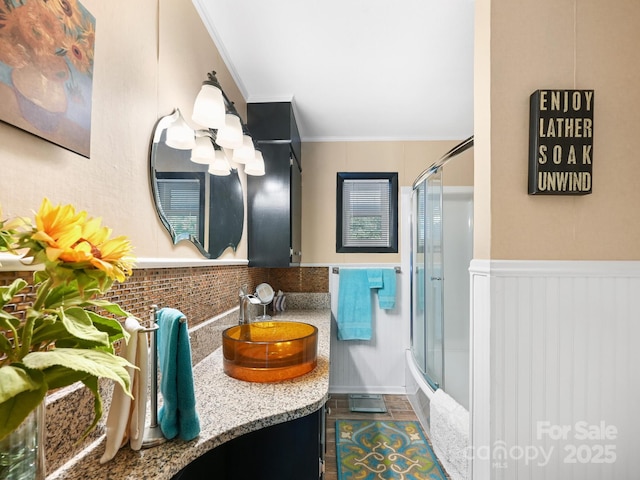 full bath featuring bath / shower combo with glass door, crown molding, tile patterned floors, vanity, and wainscoting