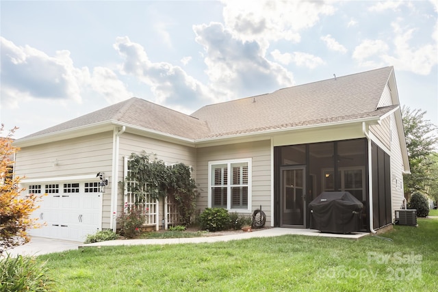 view of front of property featuring a front lawn, a sunroom, a garage, and cooling unit