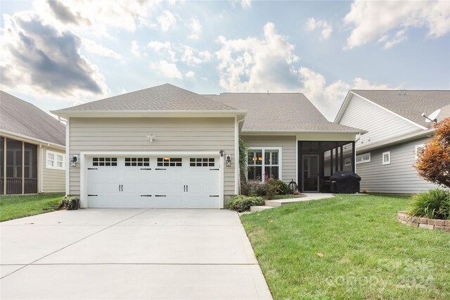 view of front of property featuring a sunroom, a garage, and a front lawn