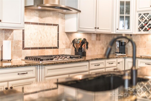 kitchen featuring wall chimney range hood, tasteful backsplash, and white cabinetry