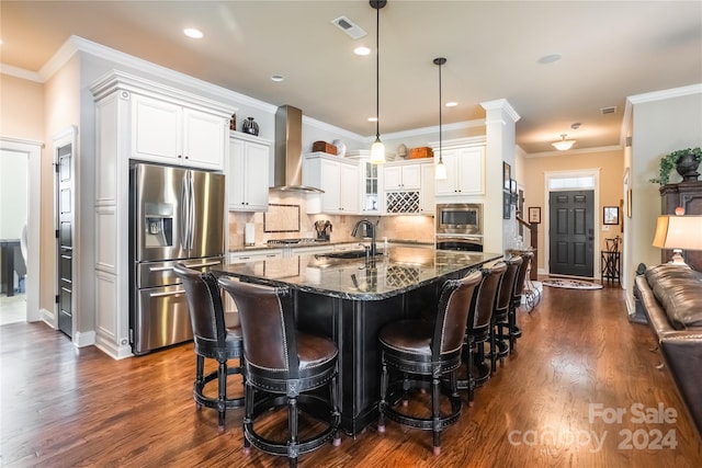 kitchen featuring a breakfast bar area, visible vents, appliances with stainless steel finishes, a sink, and wall chimney range hood