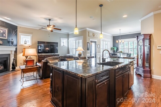 kitchen with sink, dark stone countertops, wood-type flooring, an island with sink, and ceiling fan with notable chandelier