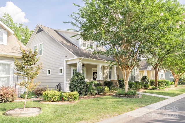 view of front of house featuring covered porch, a shingled roof, and a front yard