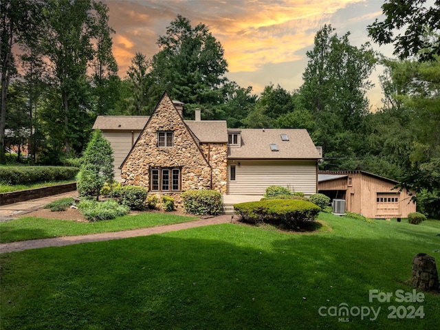 tudor house featuring stone siding, a chimney, a yard, and roof with shingles