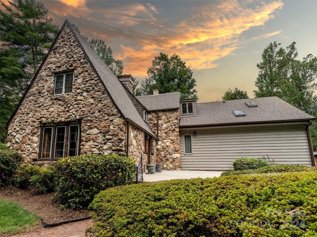 back of property with a patio area, stone siding, a chimney, and roof with shingles