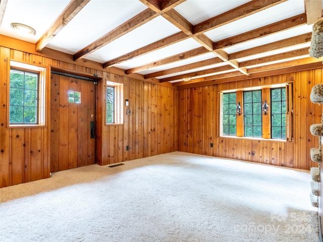 carpeted empty room featuring beamed ceiling, coffered ceiling, and wooden walls