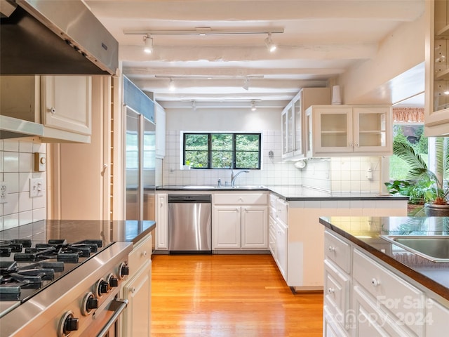 kitchen with light wood-type flooring, stainless steel dishwasher, white cabinetry, beamed ceiling, and decorative backsplash