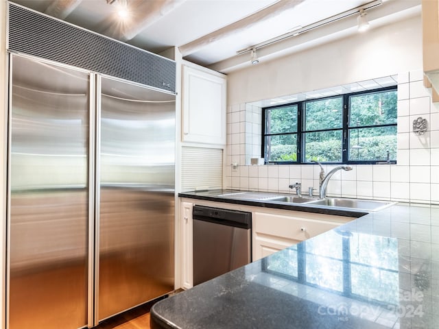 kitchen featuring appliances with stainless steel finishes, white cabinets, track lighting, backsplash, and sink