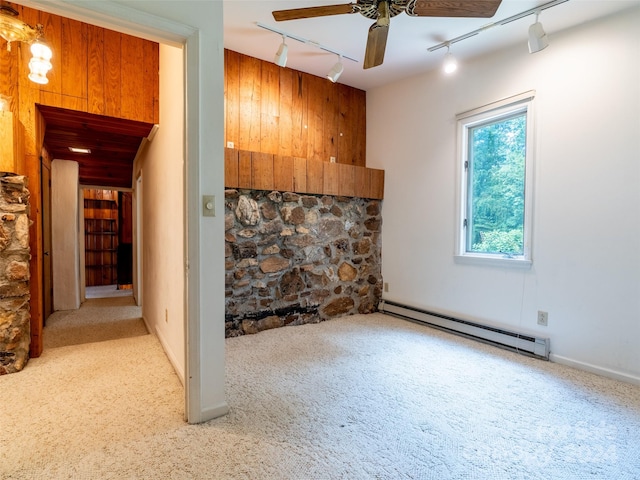 unfurnished living room with ceiling fan, wood walls, baseboard heating, and carpet