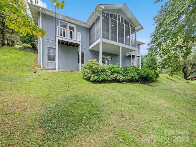 rear view of property featuring a balcony, a sunroom, and a yard