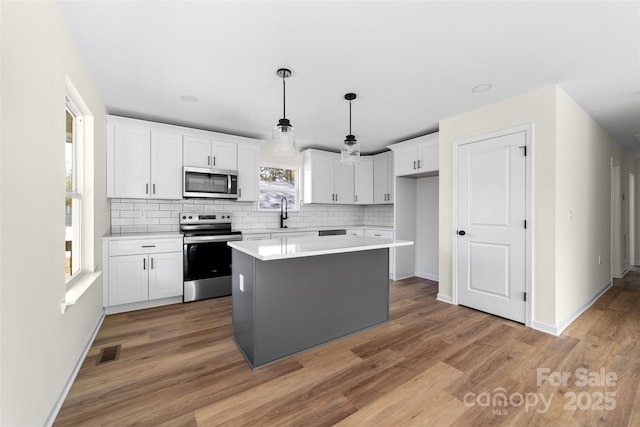 kitchen featuring white cabinets, appliances with stainless steel finishes, decorative backsplash, and a kitchen island