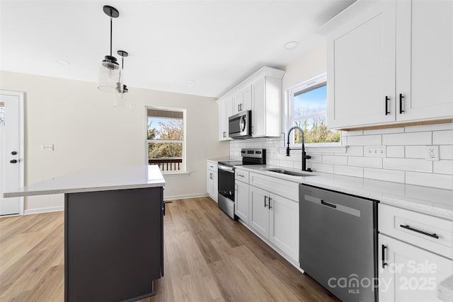 kitchen featuring stainless steel appliances, sink, white cabinets, a center island, and hanging light fixtures