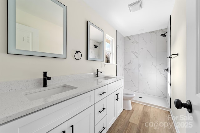 bathroom featuring tiled shower, wood-type flooring, vanity, and toilet