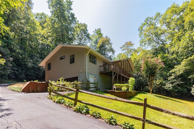 view of home's exterior with aphalt driveway, a lawn, a deck, and fence