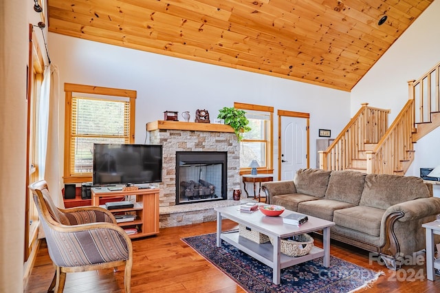 living room featuring light wood-type flooring, a stone fireplace, a wealth of natural light, and wood ceiling