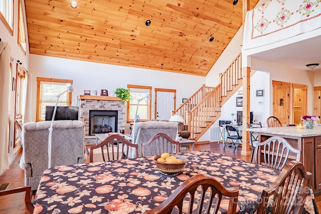 dining area with a fireplace, hardwood / wood-style flooring, high vaulted ceiling, and wooden ceiling