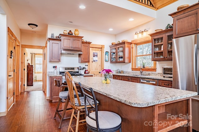 kitchen featuring a kitchen breakfast bar, sink, appliances with stainless steel finishes, a kitchen island, and dark hardwood / wood-style flooring