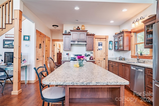 kitchen with light stone countertops, stainless steel appliances, sink, a center island, and dark hardwood / wood-style floors