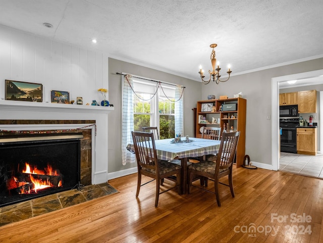 dining space with a textured ceiling, crown molding, a fireplace, an inviting chandelier, and light wood-type flooring