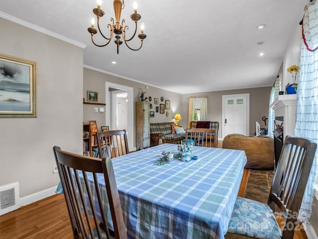 dining area with a fireplace, hardwood / wood-style flooring, a chandelier, and ornamental molding