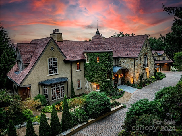 view of front of home with a chimney, stucco siding, a garage, stone siding, and driveway