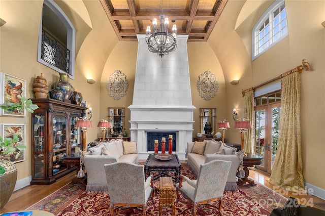 living room with coffered ceiling, a high ceiling, a fireplace, and wood finished floors