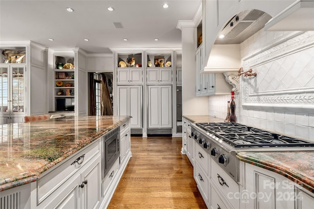 kitchen featuring light wood finished floors, glass insert cabinets, appliances with stainless steel finishes, white cabinetry, and dark stone countertops