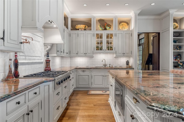 kitchen with stainless steel appliances, a sink, white cabinets, dark stone countertops, and glass insert cabinets