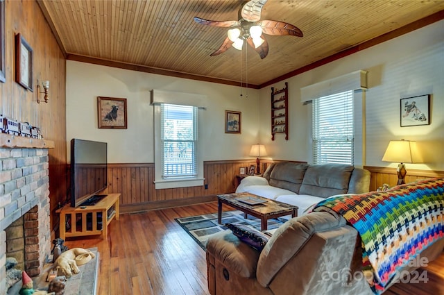 living room featuring ornamental molding, a fireplace, wood-type flooring, wooden walls, and ceiling fan