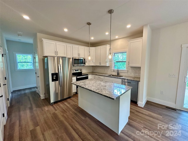 kitchen with dark hardwood / wood-style flooring, stainless steel appliances, light stone counters, a center island, and plenty of natural light