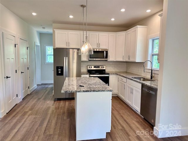 kitchen with appliances with stainless steel finishes, pendant lighting, a center island, sink, and wood-type flooring