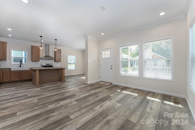 kitchen with wall chimney range hood, tasteful backsplash, hardwood / wood-style floors, ornamental molding, and decorative light fixtures