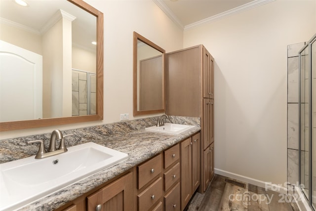 bathroom with double sink vanity, a shower with shower door, crown molding, and wood-type flooring