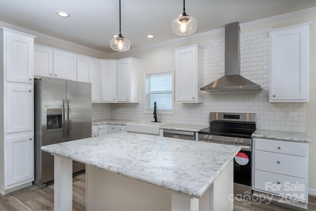 kitchen with appliances with stainless steel finishes, backsplash, wall chimney exhaust hood, a center island, and hanging light fixtures