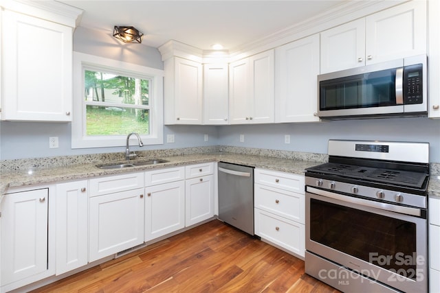 kitchen featuring hardwood / wood-style floors, white cabinets, appliances with stainless steel finishes, sink, and light stone counters