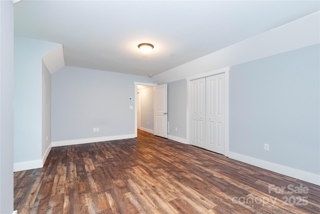 unfurnished bedroom with vaulted ceiling, a closet, and dark hardwood / wood-style flooring