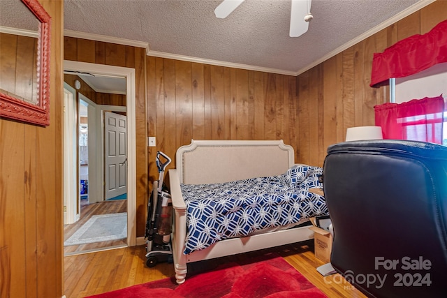 bedroom featuring wood walls, crown molding, a textured ceiling, and wood finished floors