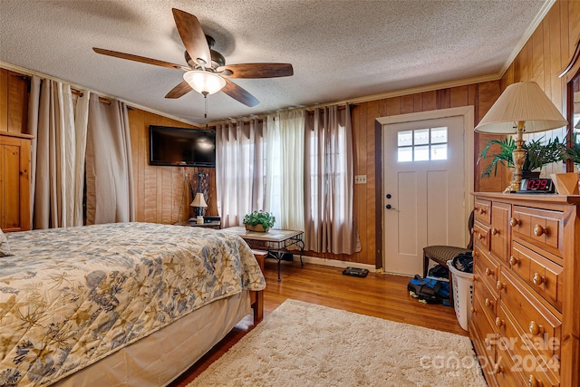 bedroom with a textured ceiling, ornamental molding, wood walls, and wood finished floors