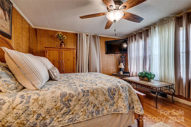 bedroom featuring a textured ceiling, wooden walls, a ceiling fan, ornamental molding, and light wood-type flooring