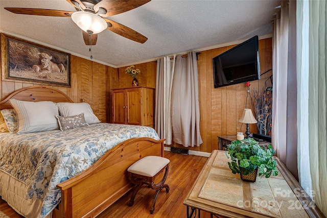 bedroom featuring crown molding, wood walls, a textured ceiling, and wood finished floors