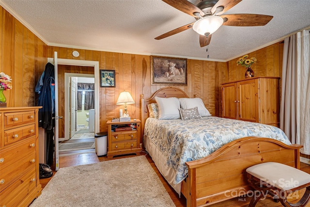 bedroom featuring a textured ceiling, wooden walls, wood finished floors, and crown molding