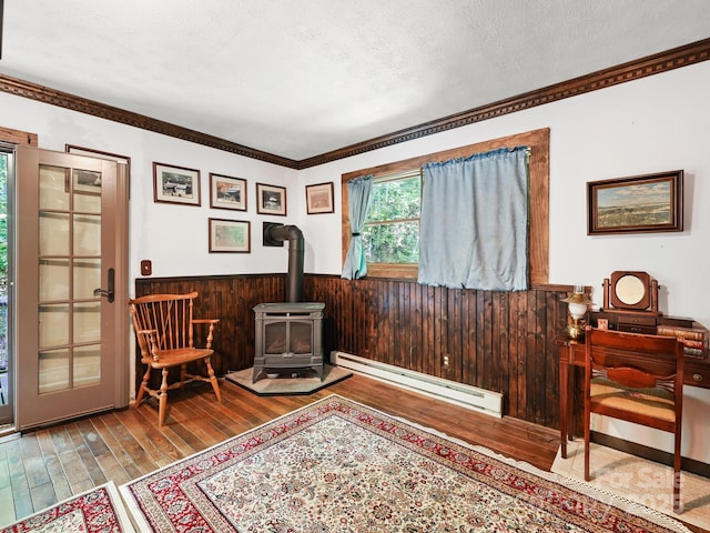 living area featuring wooden walls, a baseboard radiator, a wood stove, hardwood / wood-style flooring, and a textured ceiling