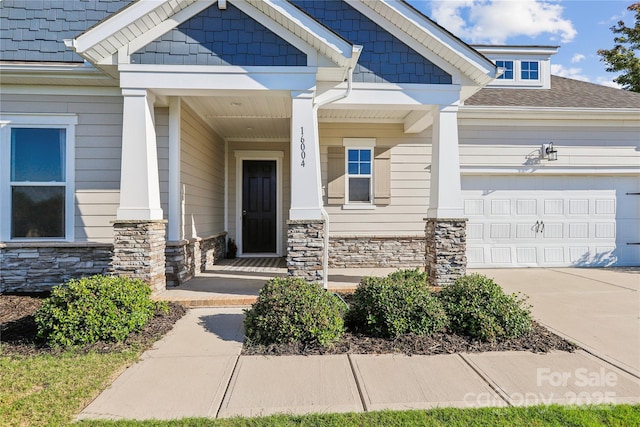 doorway to property with an attached garage, stone siding, and concrete driveway