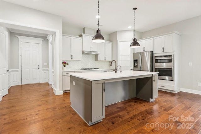 kitchen with stainless steel appliances, light countertops, a kitchen island with sink, white cabinets, and under cabinet range hood