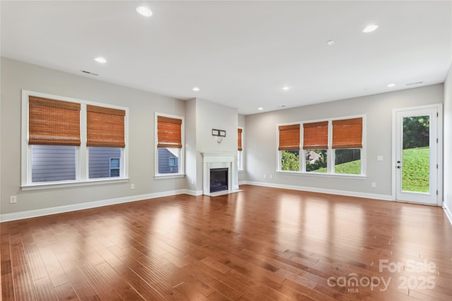 unfurnished living room with recessed lighting, a fireplace with flush hearth, wood finished floors, baseboards, and visible vents