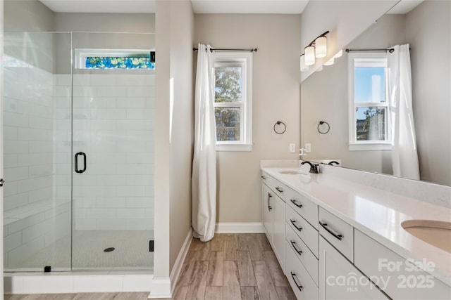 full bathroom featuring wood finished floors, a sink, baseboards, a shower stall, and double vanity