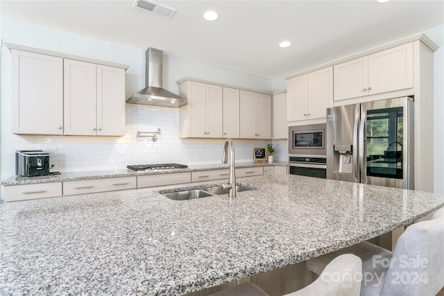 kitchen featuring light stone counters, stainless steel appliances, wall chimney exhaust hood, and a kitchen breakfast bar