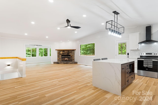 kitchen with light hardwood / wood-style floors, decorative backsplash, wall chimney exhaust hood, light stone countertops, and stainless steel electric stove